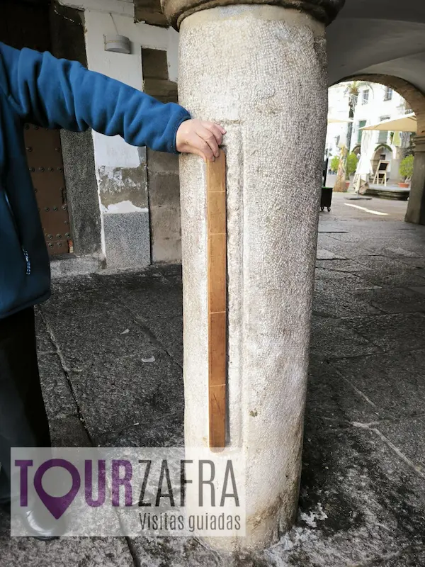 Turista comprobando la medida de una vara familiar en la Vara de Medir de la Plaza Chica de Zafra.